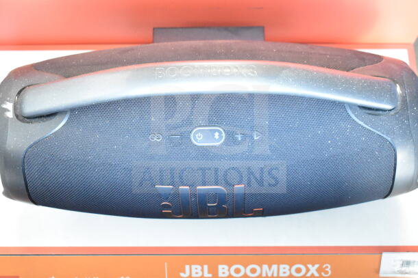 JBL Boombox 3 speaker on store display, featuring central controls and handle. Dust visible on surface.