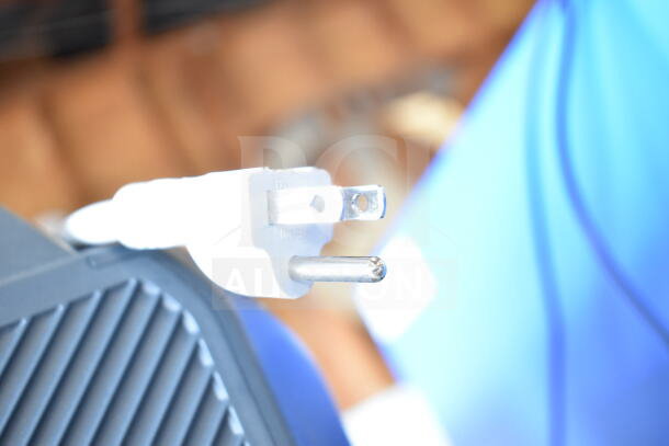 Close-up of a white European plug connected to a black speaker grill. Background shows blurred blue tones.