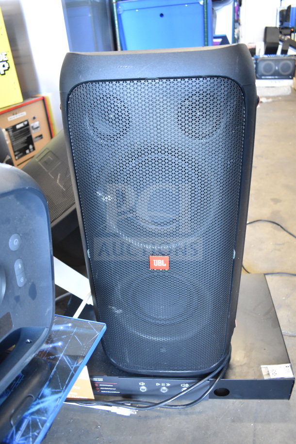 JBL PartyBox310 speaker on store display stand, in good condition. Features include grille design and visible control panel.