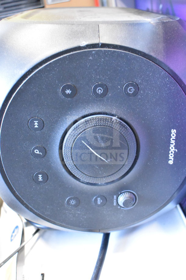 Soundcore speaker close-up showing control panel, brand logo, and buttons. Slight wear visible on the surface.