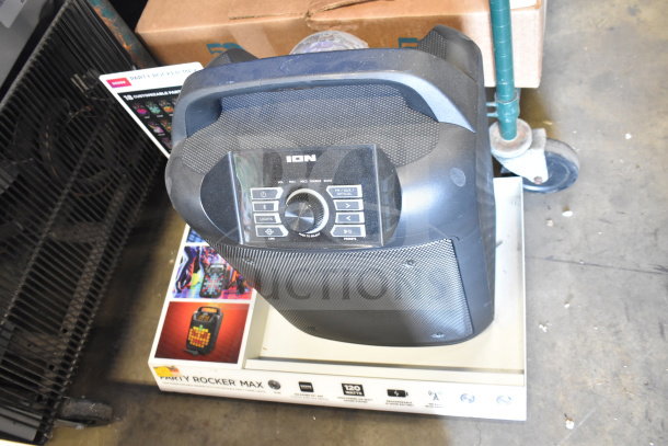 Ion speaker on display with control panel visible, showing buttons for volume, mic, source, and lights. Speaker mounted on box labeled "Party Rocker Max," featuring 120 watts and Bluetooth connectivity.