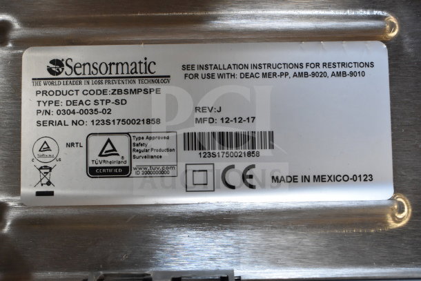 Sensormatic DEAC STP-SD label with product details, serial number, and TÜV certification. Engraved on metallic surface. Made in Mexico.