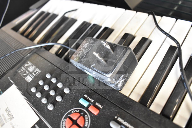 Electronic keyboard with power adapter, showing buttons for demo, play, and volume. Slight wear visible on keys.