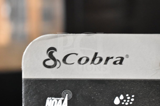 Cobra product box section, highlighting logo and NOAA hazard symbols, for item auction including keyboard, Lego, and walkie talkies.