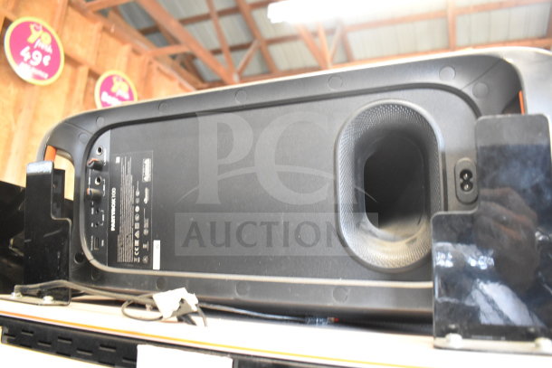 JBL PartyBox 100 speaker on store display. Features bass ports, connectivity panel, and branded labels. Good condition.