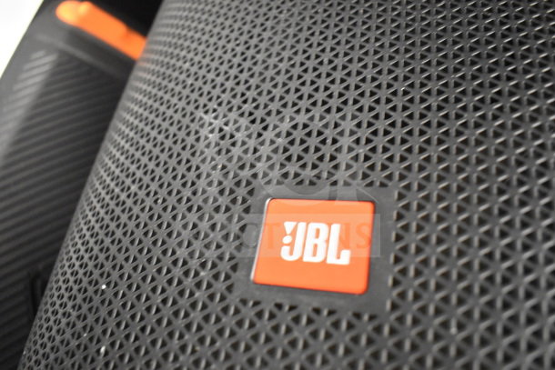 JBL speaker close-up with a textured black grille and orange JBL logo. Part of a 5-store display set.