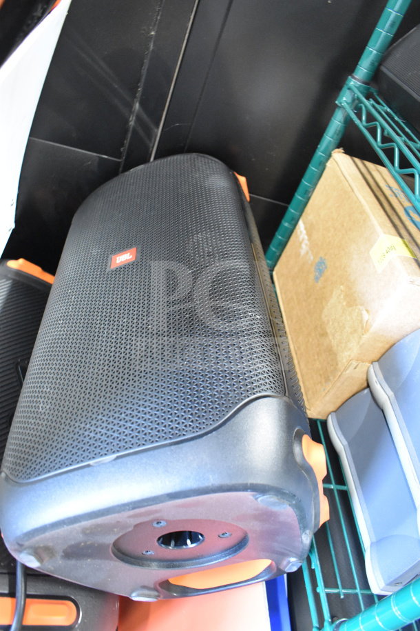 JBL speaker on a metal shelf, part of a store display auction lot. Black with orange accents, model and condition unspecified.
