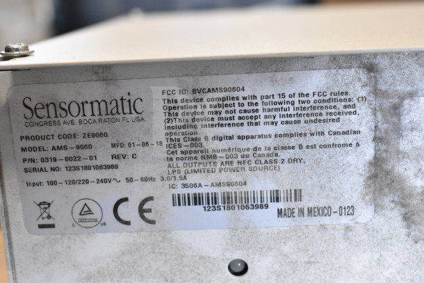 Sensormatic AMS-9060 surveillance controller, product code ZE9060. Visible label with specs, FCC and IC compliance details.
