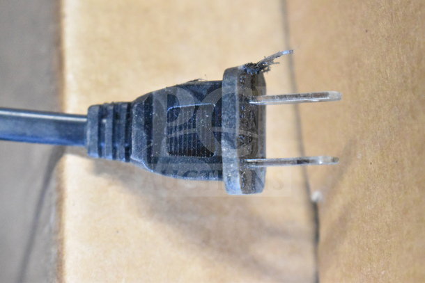 Close-up view of a frayed black power plug on a cardboard surface, part of store displays auction.