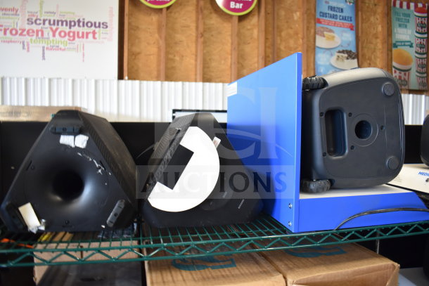 Three store displays featuring a Samsung speaker, an Onn large party speaker, and a blue display stand, on a metal shelf.