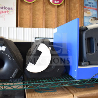 Three store displays featuring a Samsung speaker, an Onn large party speaker, and a blue display stand, on a metal shelf.