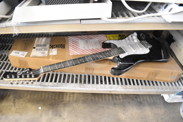 Rock Jam electric guitar, black and white, with six strings. Minor scuffs visible. Includes original packaging box.