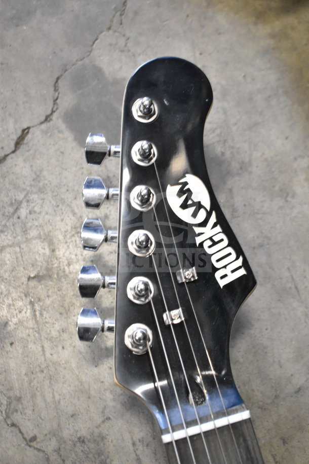 Rock Jam guitar headstock with logo, chrome tuning pegs, black finish. Part of auction lot, condition looks well-maintained.