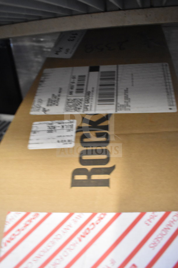 Cardboard box labeled "ROCK" containing various items including a Rock Jam guitar. Shipping labels and markings visible.