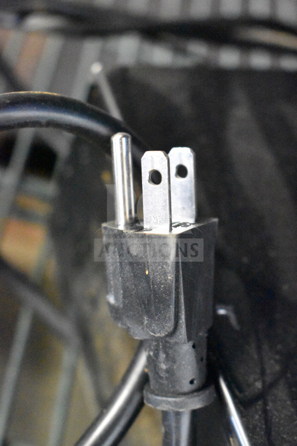 Close-up of a power plug connected to a JBL speaker store display, showing metal prongs and black cable.