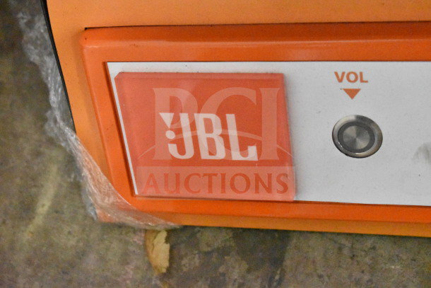 JBL PartyBox 110 Speaker display, showcasing orange JBL logo and volume control button, wrapped in protective plastic, excellent condition.