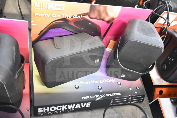 Altec Lansing Shockwave speaker display, includes two black portable speakers. Tagline: "Party On The Go!" and "Feel the BOOM!"