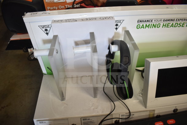 Store display featuring Turtle Beach gaming headset, LG soundbar, and screen. Signs of use; headset mounted on stand.