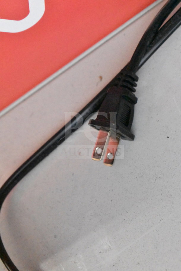 Close-up of a two-prong power cable plug on a white surface with a red background.