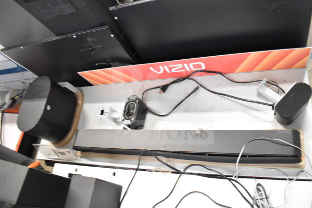 3 store display with gaming screen, headphones, LG soundbar. Includes Vizio branding. Cables and components visible.