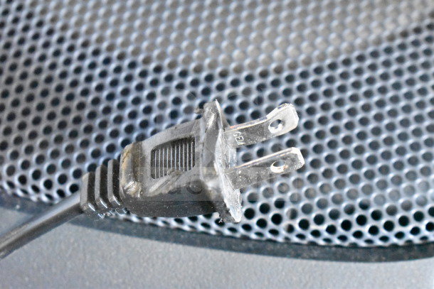 Onn Large Party Speaker plug with metal prongs on a perforated grille background, indicating electrical connectivity.