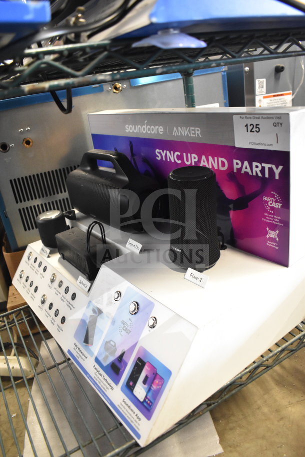 Store display featuring Soundcore Anker speakers, including Select Pro and Flare 2 models. Display promotes PartyCast technology.