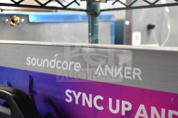 Store display featuring Soundcore Anker branding and speaker, showcasing "SYNC UP AND..." slogan. Bright and colorful design.