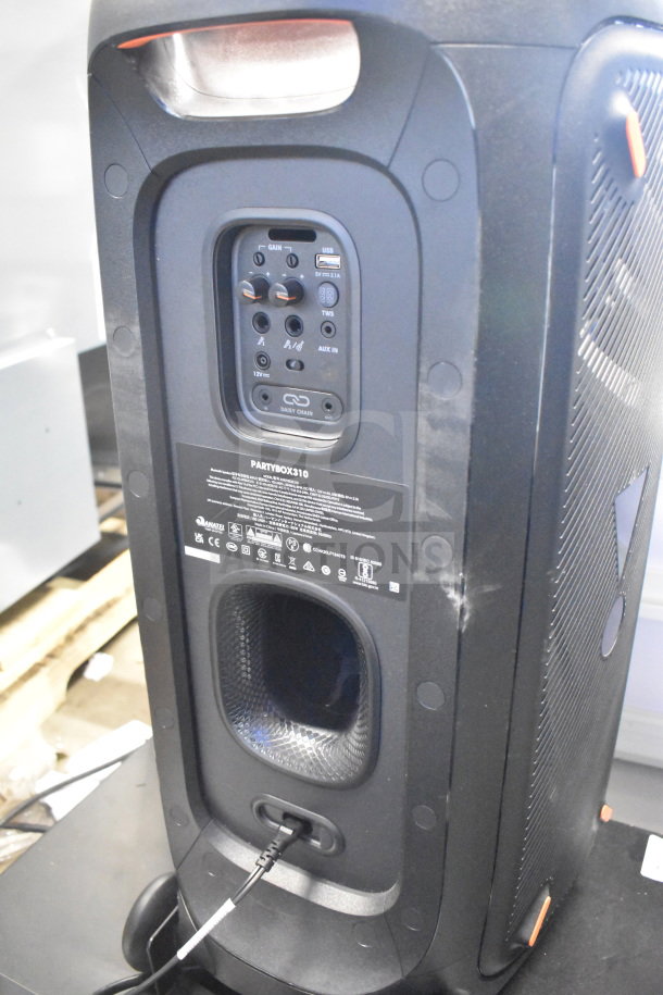 JBL Partybox 310 speaker in store display; features control panel, USB, AUX inputs, and wheels; condition appears excellent.