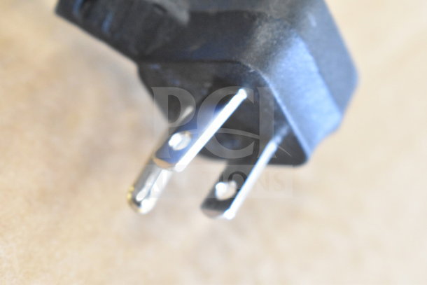 Close-up of a power plug prong from a store display with headphones, soundbar, and speaker.
