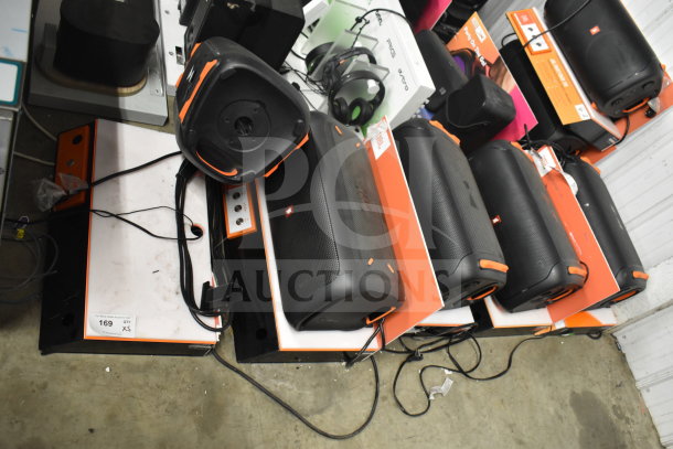 Five JBL speakers displayed on store shelves, each in good condition, with visible cords and JBL branding.