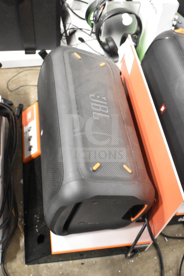 JBL speaker on display stand, black with orange accents, slightly used. Part of a 5-item store display auction.