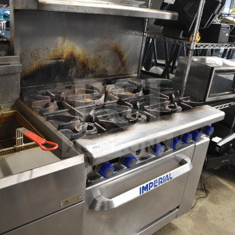 Imperial Commercial 6-burner gas range with oven, over shelf, and backsplash. Used condition, visible wear on surfaces.