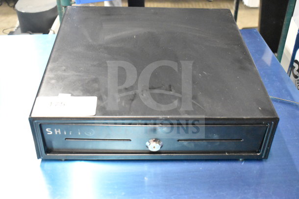 Black cash drawer with a metal front, secure key lock, and label marked "SH". Minor surface wear visible.