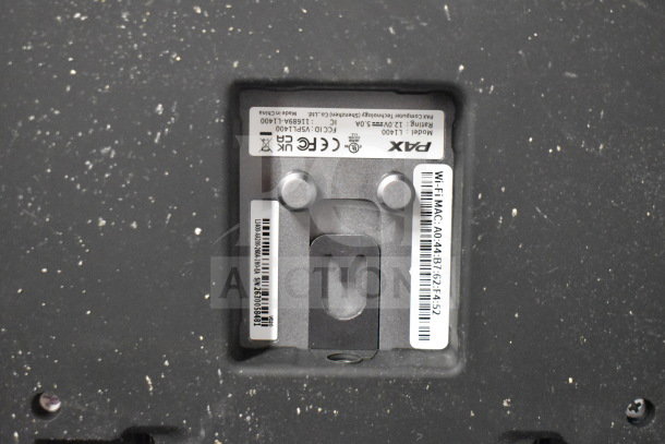 Pax L1400 POS monitor close-up showing model label and Wi-Fi MAC address on a textured surface.