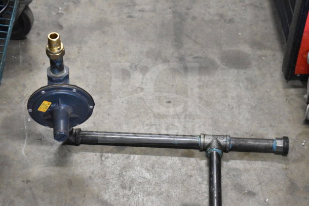 Four assorted industrial pipes on a concrete floor, featuring brass fittings and visible blue markings on a valve.