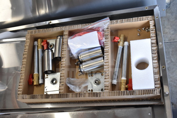 Box of components for ServIt 423EST4WSPBH steam table, including valves, pipes, and metal fixtures, shown in packaging.