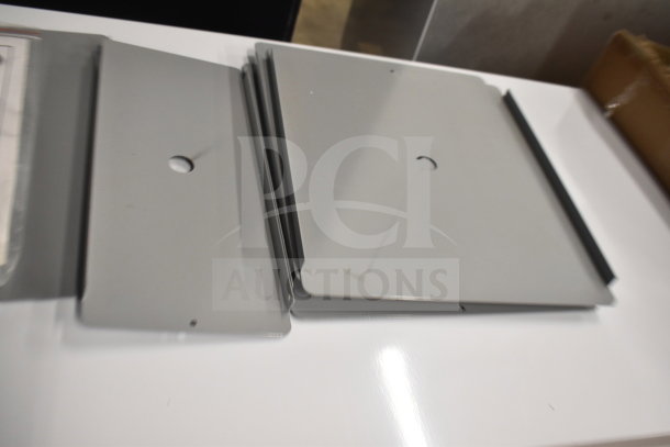Five brand new gray metal pieces, scratch and dent condition, various shapes with mounting holes, stacked on a white surface.
