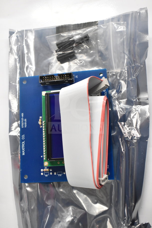 Circuit board wrapped in packaging, featuring display screen and ribbon cable. Marked "MAXITROL CO." and dated "10/21".