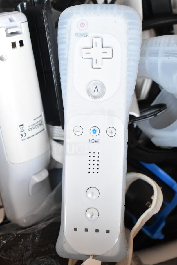 Nintendo Wii remote, white, with visible buttons, in used condition. Additional controllers and parts partially visible.