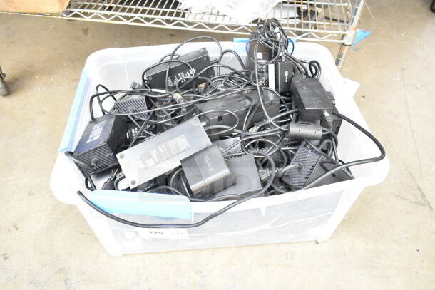 Poly bin with assorted cords and battery charger, various brands visible. Ideal for electronics salvage. Used condition.