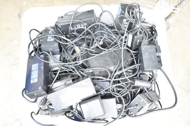 Lot of various cords and battery chargers in a clear poly bin, mixed condition, featuring multiple black adapters and cables.