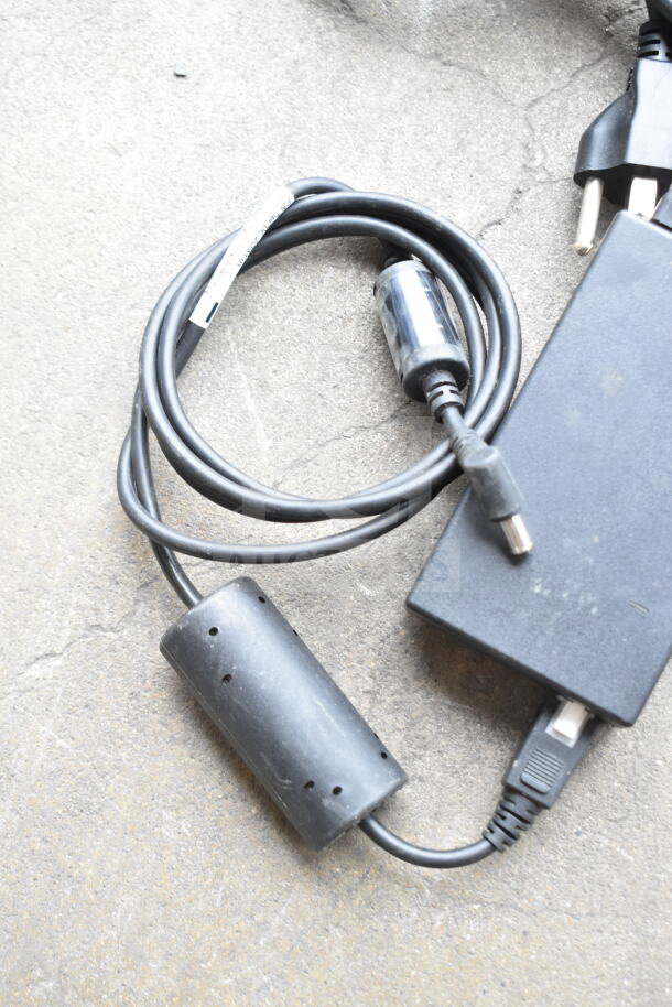 Lot of various cords and a battery charger in a clear poly bin; black insulated cables, includes plug and adapter.