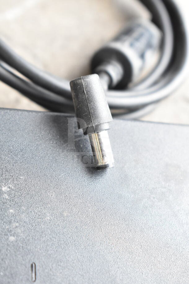 Lot of various cords and a battery charger in a clear poly bin. Includes power cables. Visible wear on surfaces.