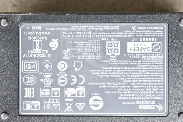 Lot of various cords and Zebra battery charger with visible safety and specification labels in a clear poly bin.
