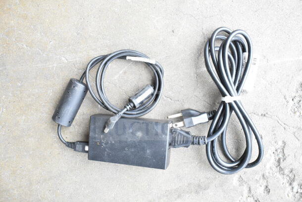 Lot of various cords and a battery charger, in used condition, displayed in a clear poly bin.