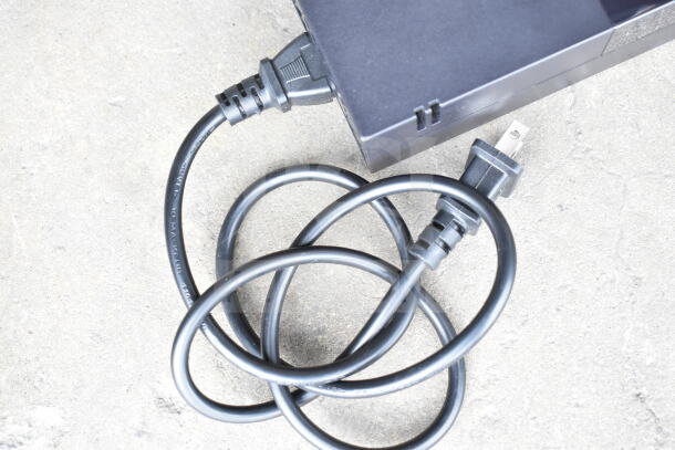 Lot of various cords and a battery charger in a clear poly bin. Cords are coiled; charger is black. Condition unknown.