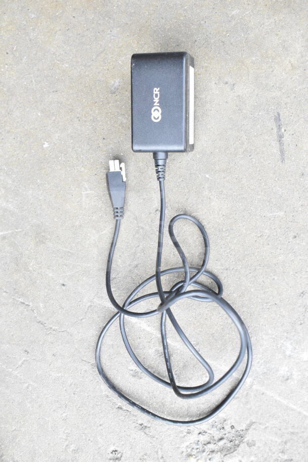 Lot of various cords and NCR battery charger in a clear poly bin, showing wear. Uses NCR branding.