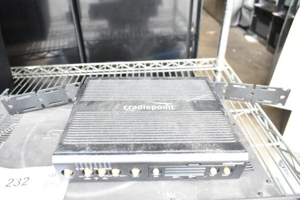 Cradlepoint AER2200 router with visible ports and mounting brackets on a metal shelf. Dust present, moderate condition.