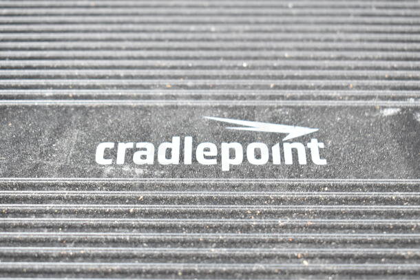 Cradlepoint AER2200 router close-up, showing logo on ribbed surface. Part of auction lot with Samson Servo 120a, SynOptics LattisHub 2814.