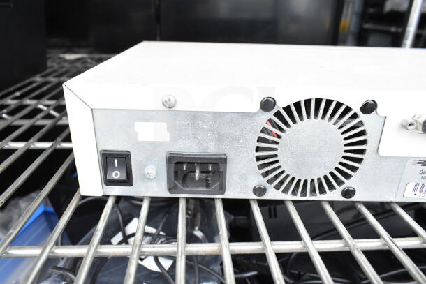 Cradlepoint AER2200, Samson Servo 120a, and SynOptics LattisHub 2814 on metal shelf. Visible power input, switch, and ventilation grille.